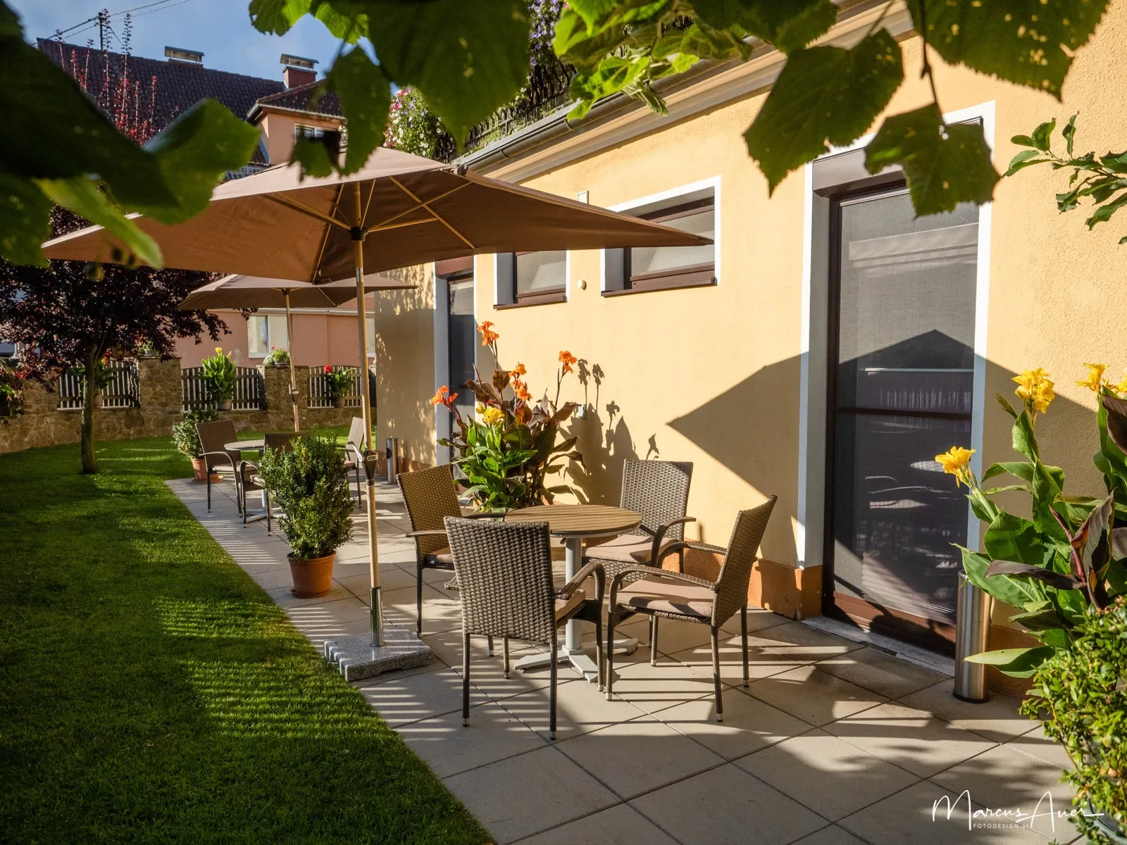 Sonnige Gartenterrasse der Pension Ehrenfried mit gedecktem Tisch, Sonnenschirm und Topfpflanzen